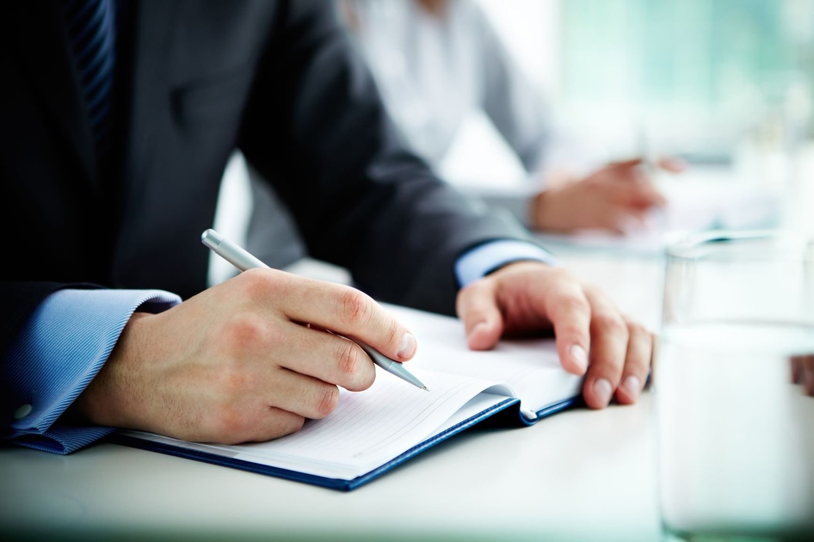 Person writing notes during a business meeting with laptop