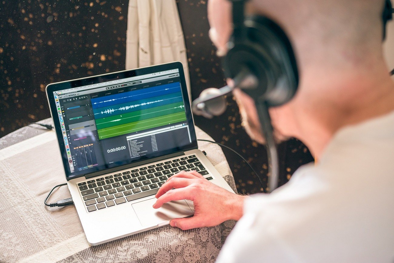 Person editing podcast audio on a computer with headphones
