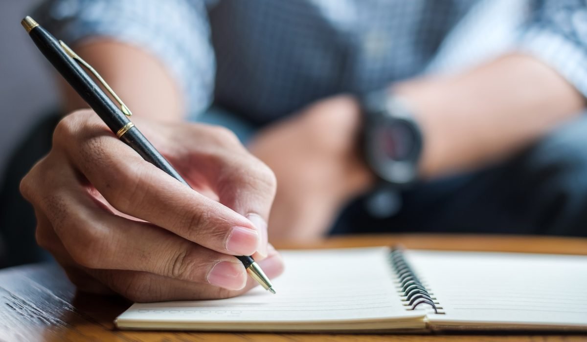 Person writing in notebook with pen